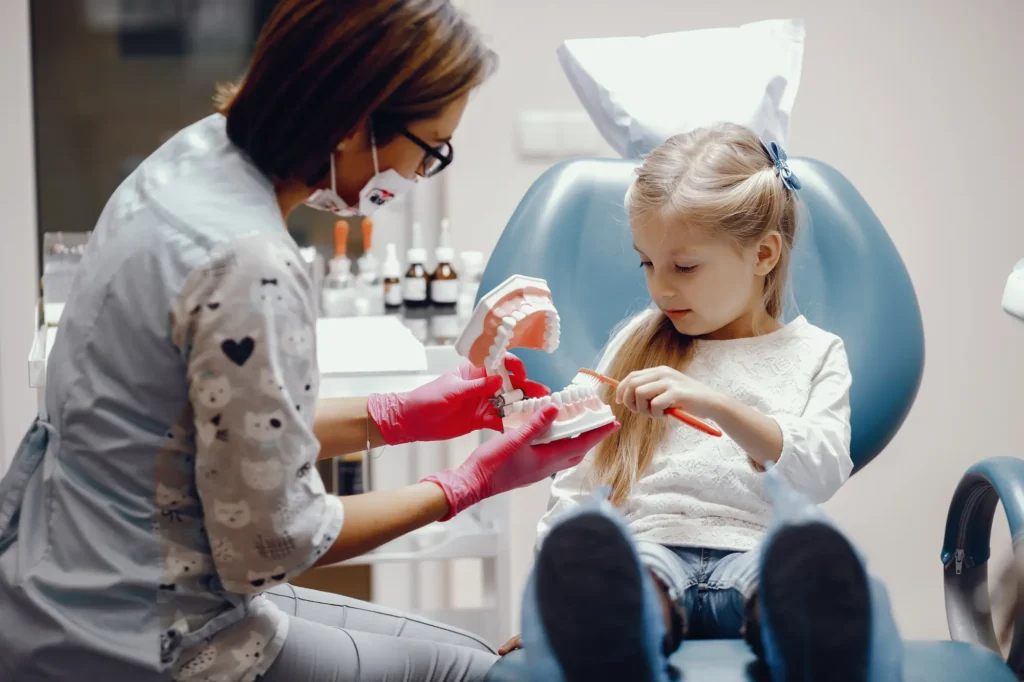 Dentist showing a young girl a model of teeth to explain oral care.